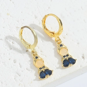 Detail of gold doll earring with blue teardrop zircon on a white stone background