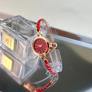 Detail of red quartz bracelet watch next to decorative perfume bottle on reflective surface