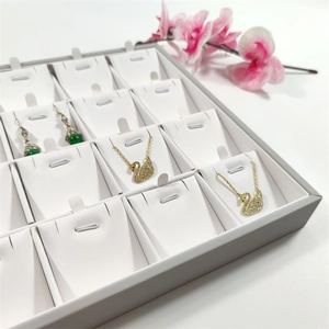 Detail view of a 24-slot jewelry display tray with white leather lining and elegant pendants