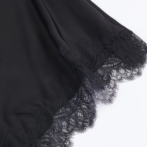 Detailed close-up of smooth black satin fabric with intricate floral lace trim on hem