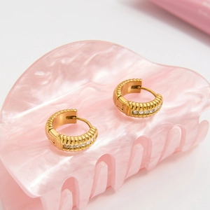 Dettaglio di orecchini a cerchio in acciaio dorato 18K con texture verticale e zirconi