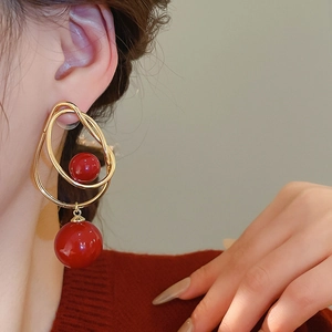 Détail de boucles d'oreilles dorées avec perles rouges portées par un mannequin élégant