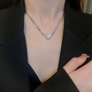 Close-up of a silver heart-shaped necklace with crystals on a layered snake chain