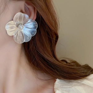 Silver metallic flower stud earrings with pearl center and brushed texture on model