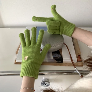 Detail of green knitted gloves featuring a small brown bear embroidery and ribbed cuffs
