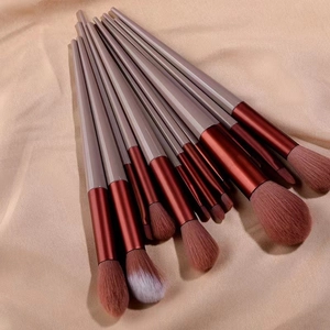 Flat lay of a 13-piece makeup brush set with burgundy gradient handles on beige fabric