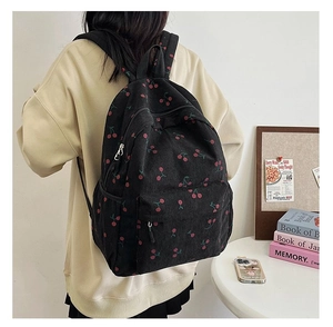 Rear view of a black corduroy backpack with cherry pattern worn in a lifestyle setting