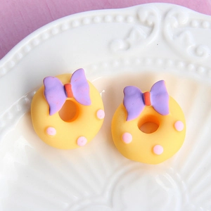Detailed close-up of a yellow donut charm with a purple bow and pink polka dots on a plate