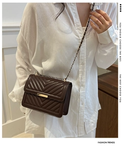 Detail of dark brown chevron quilted crossbody bag with gold metallic lock on a model