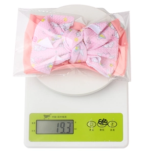 Pink nylon baby headband with heart prints on an electronic scale showing weight