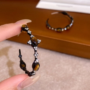 Macro shot of oval tiger eye stones and sparkling rhinestones on C-shaped hoop earrings