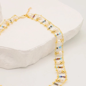 Detail of layered gold necklace with baroque pearls and colorful gemstones on white stone