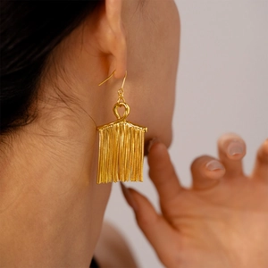 Detail of gold metal tassel earrings showing fluid movement and glossy chain texture