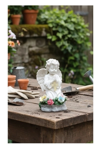 Detalle de estatua de ángel rezando en resina con cruz y rosas en un entorno de jardín