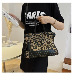 Detail of leopard print tote bag with silver studs, leather base, and black tassel charm
