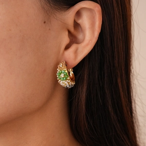 Vue macro d'une boucle d'oreille dorée en C avec des pierres vertes sur l'oreille