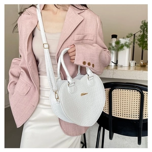 Sac blanc en forme de cœur à motif crocodile porté par un mannequin en café
