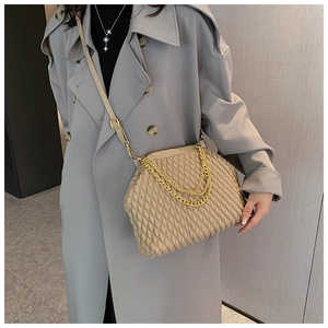 Detail of beige quilted evening bag with metal chain strap worn by a fashion model