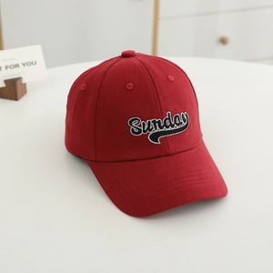 Detail of red cotton baseball cap featuring embroidered Sunday text on white surface