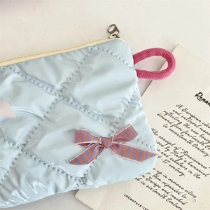 Detail of light blue quilted cosmetic bag with ribbon bow and pink braided handle