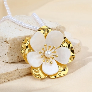 Close-up of shell flower pendant with pearl center on gold beaded necklace