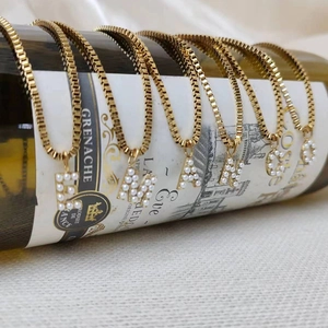 Detalle de colgantes de letras con perlas en cadenas de caja doradas sobre una botella