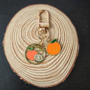 Creative orange enamel fruit keychain with gold finish on round wooden display