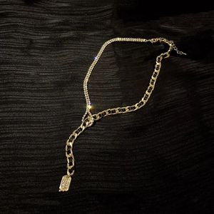 Détail du collier en Y doré avec chaîne de strass et maillons à ruban noir entrelacé