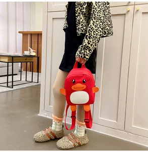 Toddler girl wearing a cute red cartoon duck canvas backpack in a bright indoor home setting