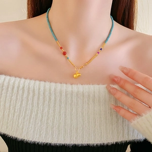 Detail of beaded necklace with gold gourd pendant on model in white sweater