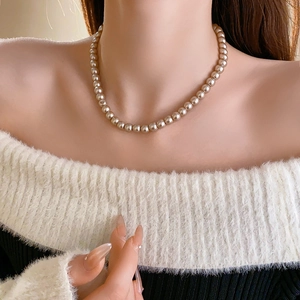 Detail of elegant beige pearl choker necklace worn on a female model with white top