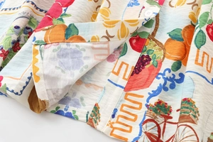 Close-up of vibrant fruit print and button detail on textured cotton-linen fabric