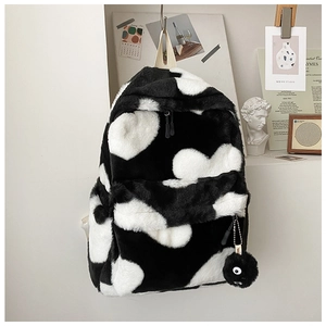 Detail of soft plush cow print backpack featuring a cute black fuzzy sprite charm