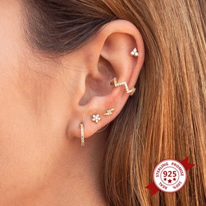 Macro view of gold-plated 925 silver stud earrings set on ear with flower and star designs