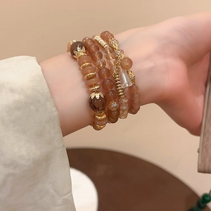 Detail of multi-layer beaded bracelets in amber and gold worn on a female wrist