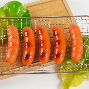 Realistische künstliche Grillwürste auf einem Metallrost mit Dekosalat auf einem Tablett