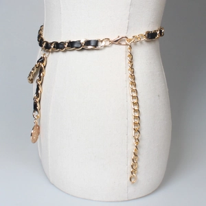 Detail view of gold metal chain woven with black leather featuring a round coin charm
