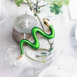 Detailed view of a green snake brooch with gold accents on a decorative glass jar