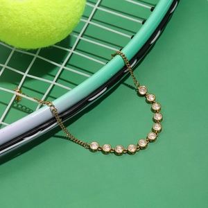 Détail d'un bracelet doré avec douze zircons sur fond de raquette de tennis vert menthe