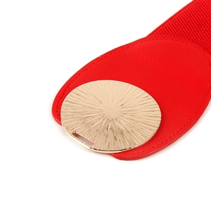 Macro view of a red elastic waist belt with a sunburst textured golden metal buckle
