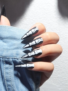 Detail of long stiletto press-on nails with black glossy finish and white bone pattern