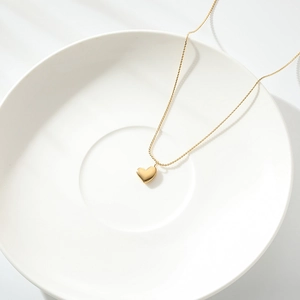 Close-up of a minimalist gold heart pendant necklace on a white ceramic dish