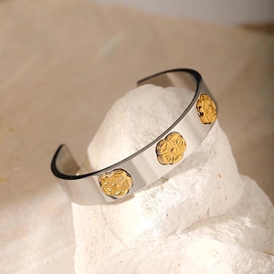 Detailed close-up of a silver open cuff bracelet featuring gold floral relief patterns