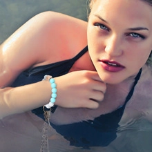 Blue and white beaded bracelet with metal keychain worn by a model in a swimming pool