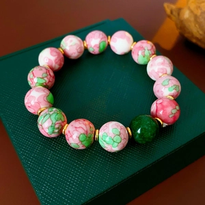 Macro detail of pink ceramic beads and golden spacers on a beaded charm bracelet