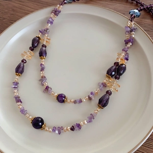 Makroaufnahme einer mehrschichtigen Amethyst-Glasperlenkette mit goldenen Trennelementen