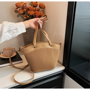 Close-up of pleated khaki faux leather bag with gold hardware and top handle detail