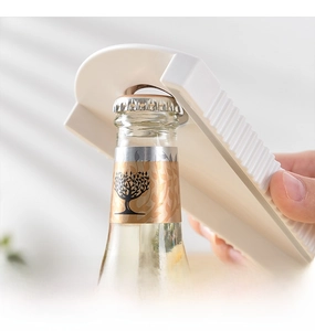 Close-up of a white multifunctional opener easily prying open a beer bottle crown cap