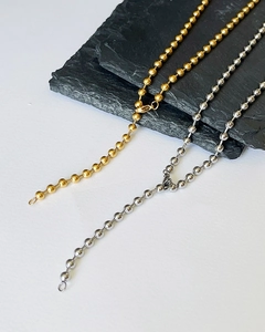 Detail of minimalist gold and silver S925 beaded chains on grey stone and white surface