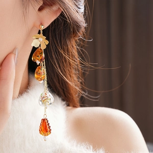 Macro detail of asymmetric amber tassel earring with floral stud worn by model